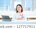 A woman in a white coat sitting at a table 127717911