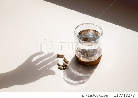 Various Capsules and Glass of Water with Hand Shadow on Light Background. Daily Vitamins and Pills for Medical Treatment. 127718278