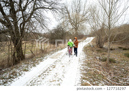 Exploring a serene winter landscape with a child riding a bicycle along a snowy path in a peaceful rural area on a chilly afternoon 127718297