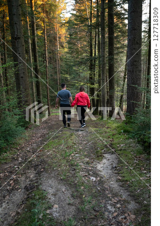 Couple enjoying a serene walk through a lush forest during golden hour, hand in hand while leaves rustle and sunlight filters through the trees Couple enjoying a serene walk through a lush forest during golden hour, hand in hand while leaves rustle and sunlight filters through the trees 127718309