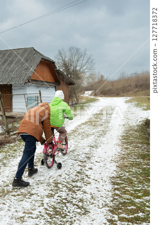 Joyful winter day as a child learns to ride a bike in snowy rural landscape with loving guidance from an adult in a charming village setting 127718372
