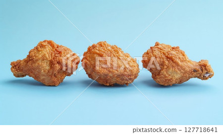 Three pieces of crispy fried chicken arranged in a row on a bright blue background, highlighting their golden-brown texture. 127718641