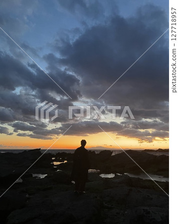 Back view of a man standing on the beach at dusk 127718957