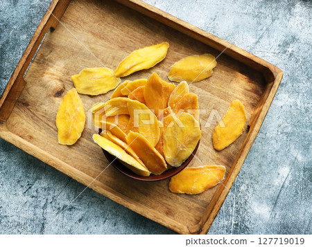 Dried mango strips in wooden bowl. Sliced, dehydrated mangoes. Juicy tropical  fruit with yellow  color. 127719019