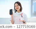 A woman in a white coat and apron holding a smartphone 127719160