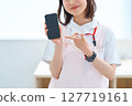 A woman in a white coat and apron holding a smartphone 127719161