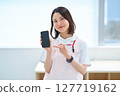 A woman in a white coat and apron holding a smartphone 127719162