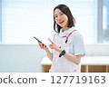 A woman in a white coat and apron holding a smartphone 127719163