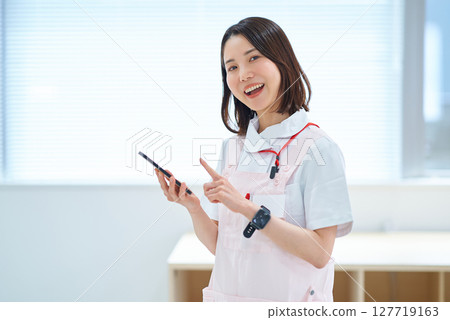 一位身穿白大褂和圍裙的女士拿著一部智慧型手機 127719163