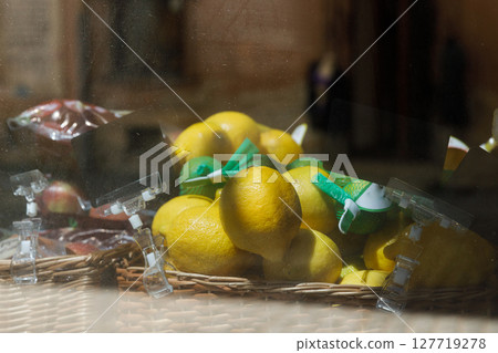 A Vibrant Display of Fresh Lemons in a Market Setting Captured Through Glass with Other Fruits in Background Showcasing Bright Yellow Color and Natural Charm A Vibrant Display of Fresh Lemons in a Market Setting Captured Through Glass with Other Fruits in Background Showcasing Bright Yellow Color and Natural Charm 127719278