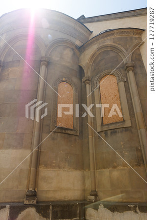 Sunlit Historical Architecture Featuring Wooden Panels Covering Windows, Showcasing Intricate Stonework on a Beautiful Historic Building in a Quaint Urban Setting 127719287