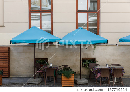 Charming Outdoor Caf Space with Bright Blue Umbrellas and Cozy Tables Ready for Guests to Enjoy Their Favorite Beverages and Meals in a Relaxed Atmosphere Charming Outdoor Caf Space with Bright Blue Umbrellas and Cozy Tables Ready for Guests to Enjoy Their Favorite Beverages and Meals in a Relaxed Atmosphere 127719324