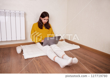 A girl is sitting on the floor in the house and working on a laptop. 127719780