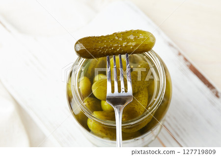 Pickled cucumbers on a fork and in a jar on a wooden background. Pickled cucumbers on a fork and in a jar on a wooden background. 127719809