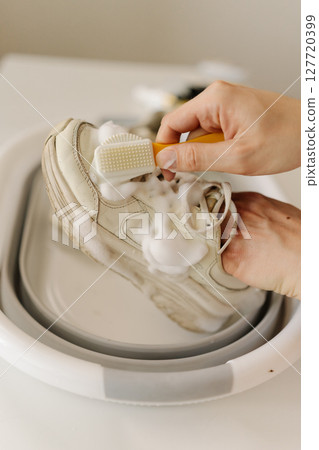 Vertical top view shot of cleaning white sneakers with small brush, removing mud stains from worn footwear in basin. Concept of hygiene, footwear free from dirt and bacteria for healthy lifestyle. Vertical top view shot of cleaning white sneakers with small brush, removing mud stains from worn footwear in basin. Concept of hygiene, footwear free from dirt and bacteria for healthy lifestyle. 127720399