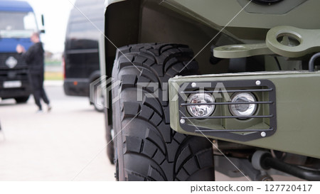 Soldiers are engaged in vehicle maintenance, focusing on the rugged tires and headlights of a military truck in a wartime environment under clear skies. 127720417