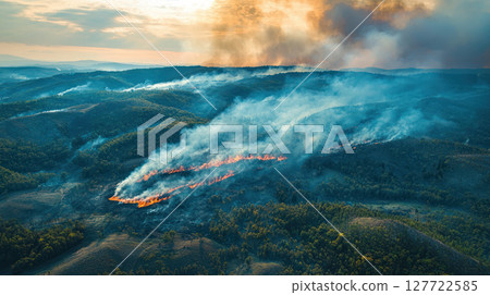 dramatic aerial view of wildfire spreading across hilly forest landscape, with smoke plumes rising high into atmosphere 127722585