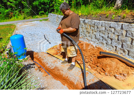 Plumber stands connect to water well working with black hose while digging in ground for plumbing system 127723677