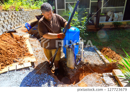 Plumber works on setting up water well pump outside, enhancing in residential area during works day 127723679