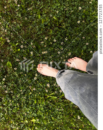 Individual is walking barefoot on vibrant green grass adorned with delicate white flowers, highlighting a serene outdoor experience and natural beauty 127723785