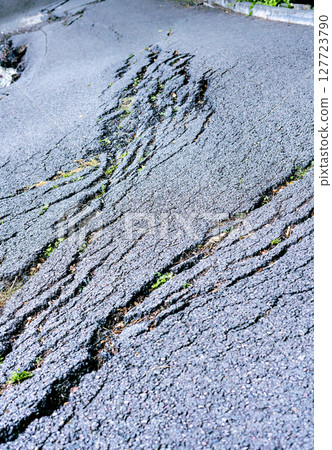 Cracked asphalt surface with visible fissures and patches of green grass, showcasing the effects of weathering and natural elements on urban infrastructure and road maintenance 127723790