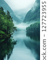 Calm misty lake surrounded by lush mountains and trees in a serene natural landscape at dawn 127723955