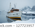 Snow-covered boat rests in tranquil harbor during winter morning in a picturesque coastal village 127723957