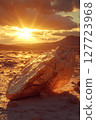 Sunrise illuminates a large rock formation in a desert landscape with mountains in the background 127723968