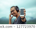 Smiling man in headphones showing a smartphone screen. 127723970