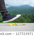 Foot stepping on a slippery banana peel on asphalt. 127723971