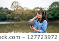 Woman relaxing with headphones and phone by a tranquil lake. 127723972