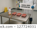 Cross Contamination Incident in Meat Packaging Plant Due to Improper Chemical Bottle Placement and Active Spill Near Raw Ground Beef Trays in Sanitation-Controlled Zone 127724031