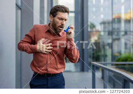 A man in an orange shirt is holding a blue inhaler. He is breathing heavily. The inhaler is blue and is in his hand A man in an orange shirt is holding a blue inhaler. He is breathing heavily. The inhaler is blue and is in his hand 127724203