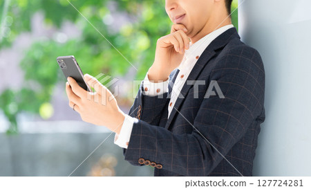 男商人一邊看著智慧型手機螢幕一邊思考 127724281