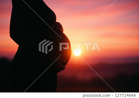 Silhouette of a pregnant woman belly glowing at a vibrant sunset or sunrise 127724649