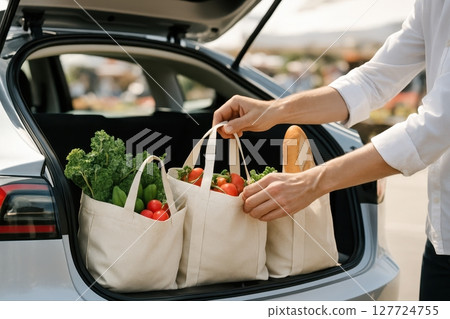 Man loading eco friendly reusable shopping bags with fresh groceries into car trunk 127724755