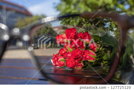 Vibrant red rose bouquet in clear wrap, seen through an obscured reflection, conveying passion, romance, and a thoughtful gesture for a special moment 127725120