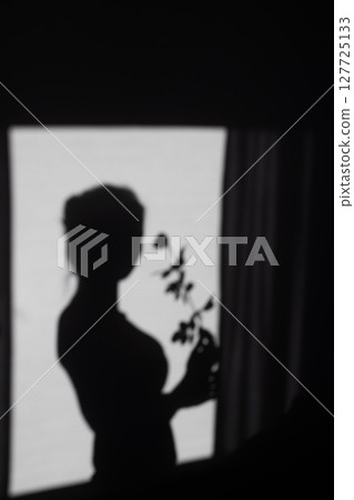 Silhouette of a graceful woman holding a delicate flower, creating a serene and artistic shadow on a bright wall, symbolizing elegance and contemplation Silhouette of a graceful woman holding a delicate flower, creating a serene and artistic shadow on a bright wall, symbolizing elegance and contemplation 127725133