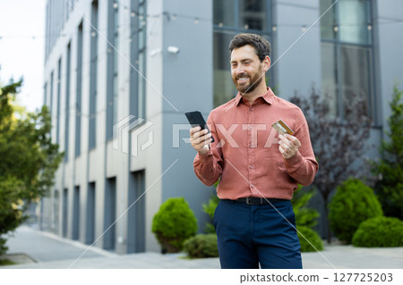 A young man in an urban environment makes use of his smartphone and credit card for seamless online shopping. A young man in an urban environment makes use of his smartphone and credit card for seamless online shopping. 127725203
