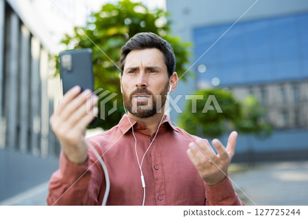 A man is actively engaged in a phone conversation outdoors while enjoying the daylight. A man is actively engaged in a phone conversation outdoors while enjoying the daylight. 127725244