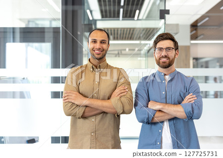 Two confident men stand in an office setting, arms crossed, smiling at the camera. They showcase a professional demeanor. Two confident men stand in an office setting, arms crossed, smiling at the camera. They showcase a professional demeanor. 127725731