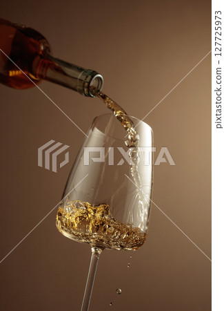 Pouring white wine from a bottle into a glass. 127725973