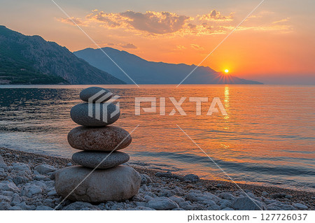 Balanced silhouette of pebble pyramid on beach at sunset. Selective focus. Abstract bokeh with sea in background. Zen stones on sea beach. 127726037