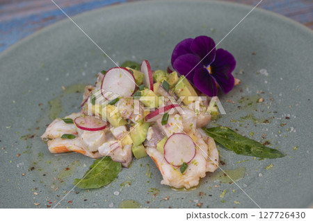 Fresh dorade and shrimp ceviche with avocado, radish, and edible flower on a decorated plate Fresh dorade and shrimp ceviche with avocado, radish, and edible flower on a decorated plate 127726430