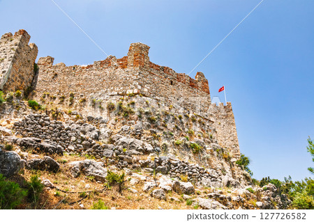 Medieval stone fortress wall with Turkish flag on top of Alanya Castle under clear blue sky Medieval stone fortress wall with Turkish flag on top of Alanya Castle under clear blue sky 127726582