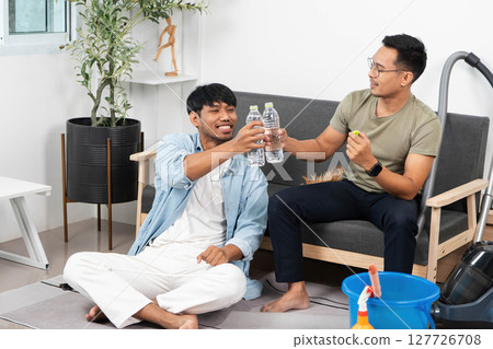 Friendship and Celebration. Two men toasting with water bottles while relaxing at home. 127726708