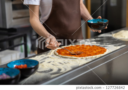 Female cooker putting filling into pizza in the kitchen 127726842