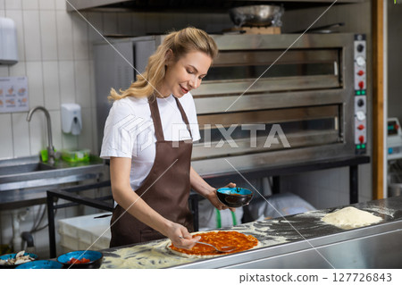 Female cooker putting filling into pizza in the kitchen Female cooker putting filling into pizza in the kitchen 127726843