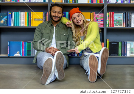 Multicultural man and woman sitting on floor in library 127727352