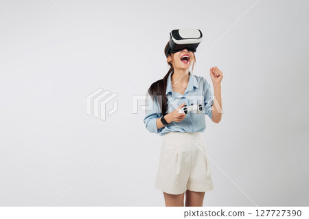 Game becomes real as Excited young Asian woman in VR headset plays console game, fully immersed in futuristic virtual dimension. isolated studio white background Game becomes real as Excited young Asian woman in VR headset plays console game, fully immersed in futuristic virtual dimension. isolated studio white background 127727390